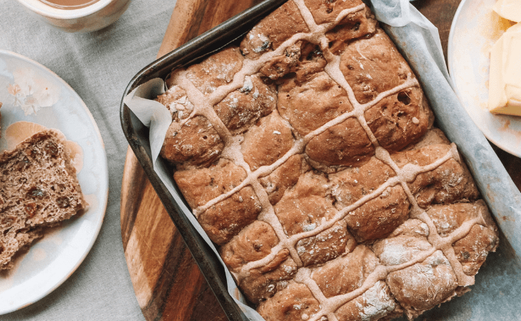 tray of hot cross buns with a plate of butter